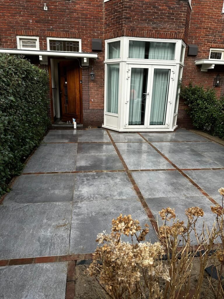 Strakke voortuinbestrating met grote grijze tegels bij woning met erker