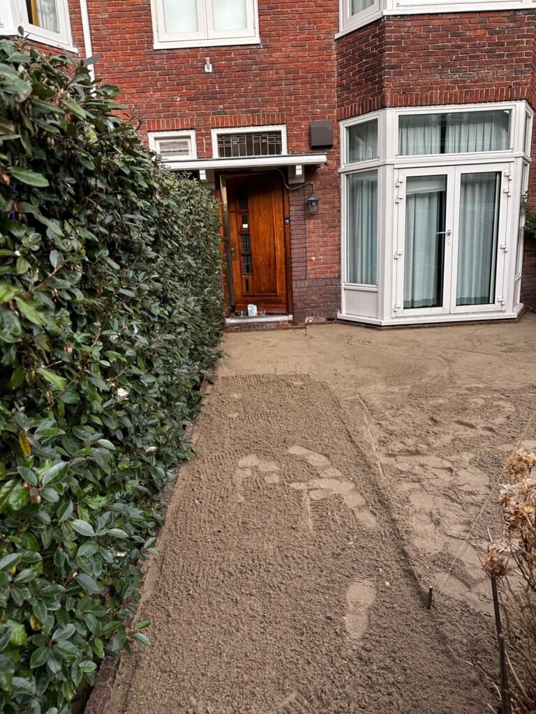 Voorbereide voortuin met geëgaliseerde ondergrond langs een haag bij een woning met bakstenen gevel