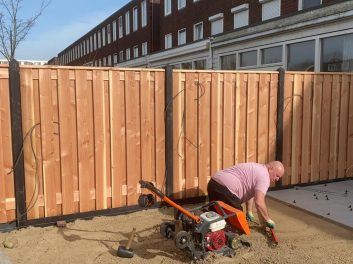 Hovenier met roze shirt op zijn knieen aan het werk in het zand in de tuin